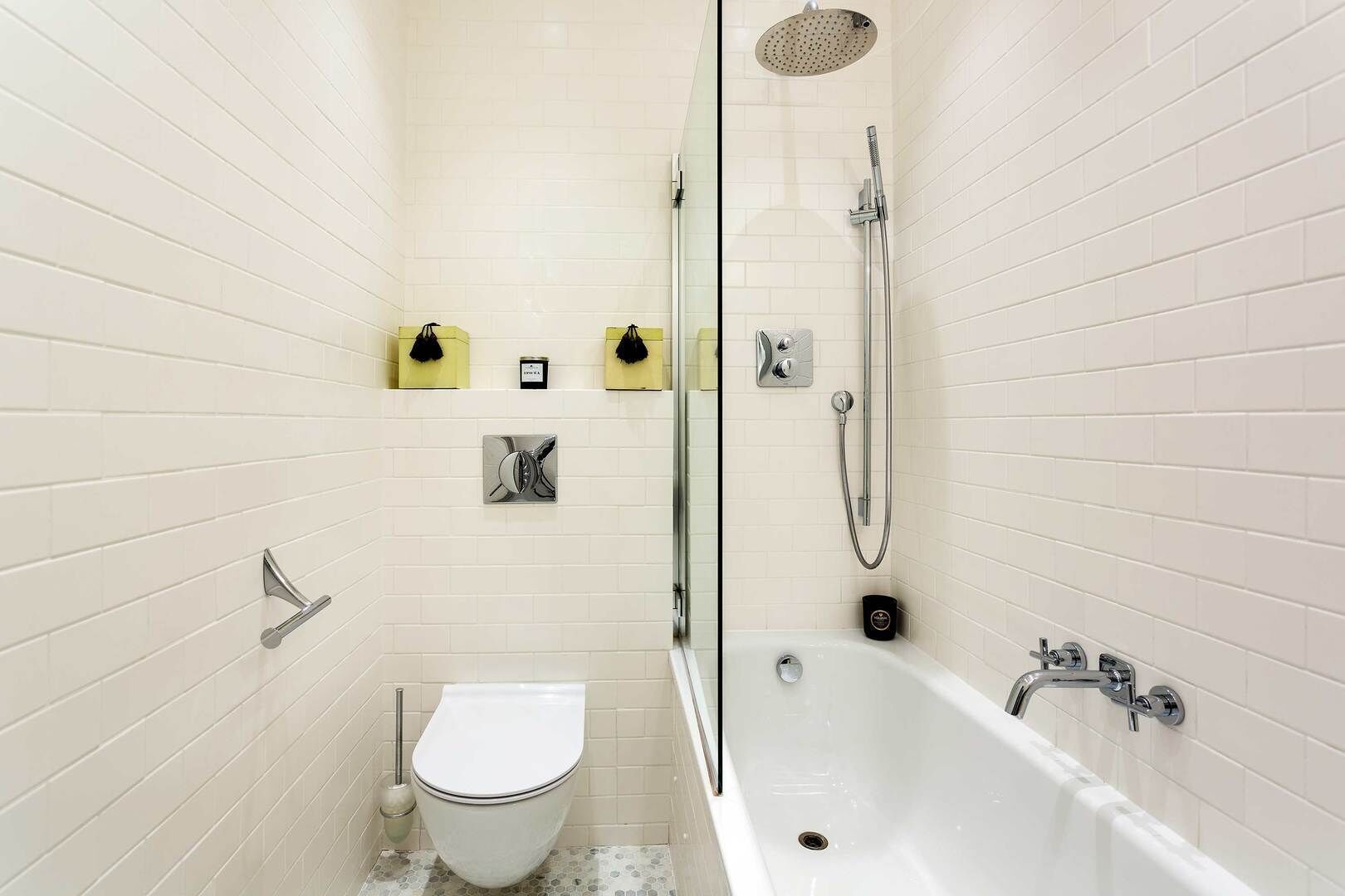 Een moderne badkamer met een betegelde muur, een douche met glazen wand, een ligbad en een toilet.