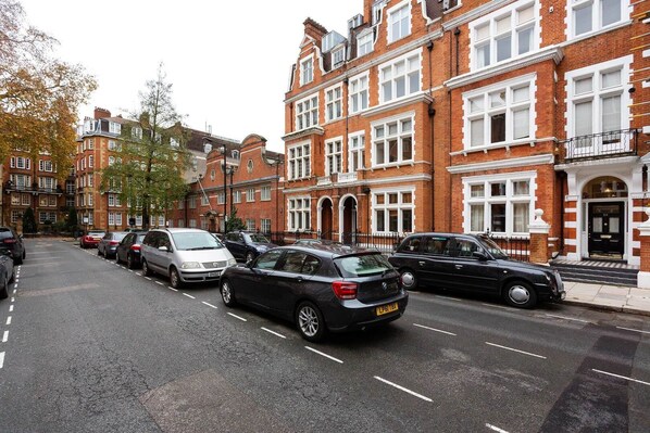 A street lined with red brick houses, parked cars, and trees with autumn leaves.