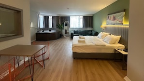 Ein Hotelzimmer mit Bett, Schreibtisch, Stuhl, Sofa, Fernseher und einem Badezimmer mit Badewanne und Spiegel.