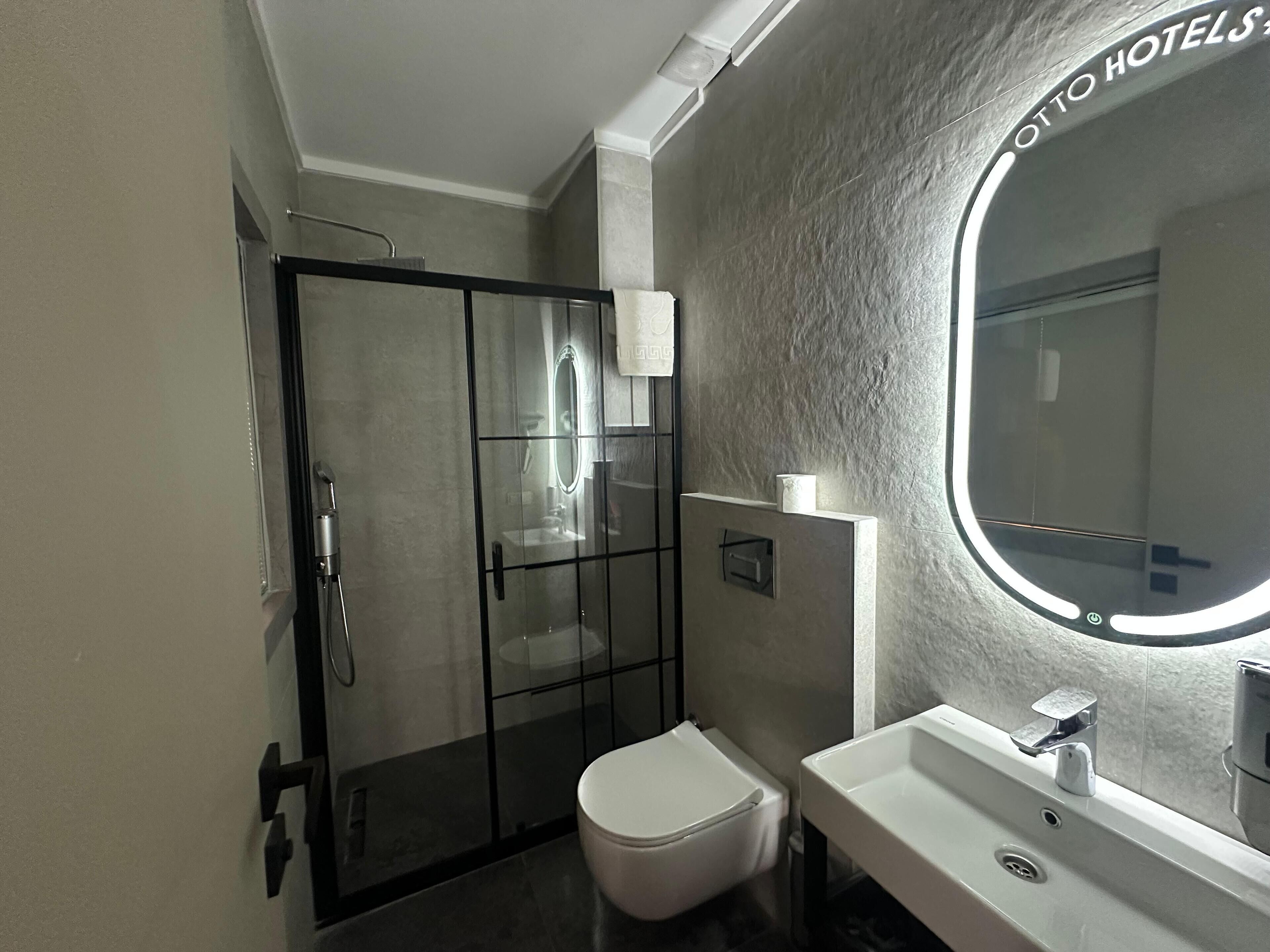 A modern bathroom with a glass-enclosed shower, a white toilet, and a sink with a mirror above it.