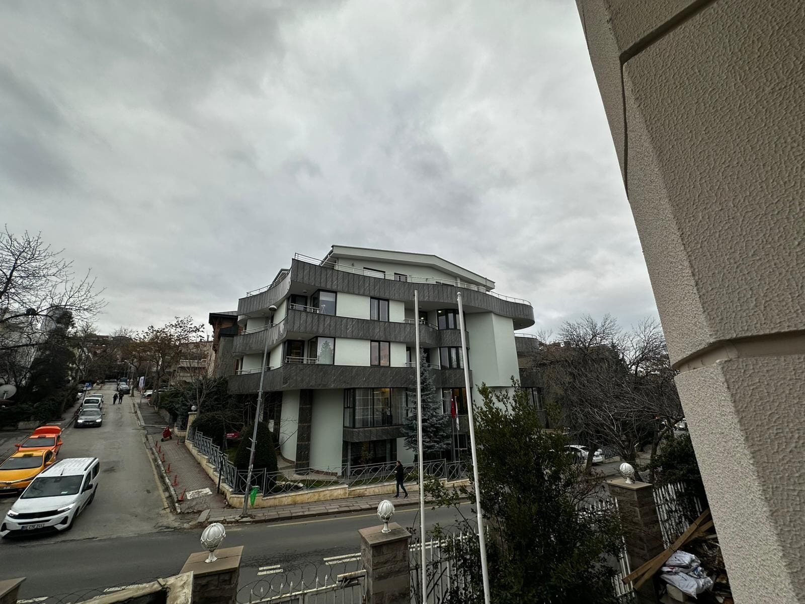 A multi-story building with balconies, a street in front, and parked cars.