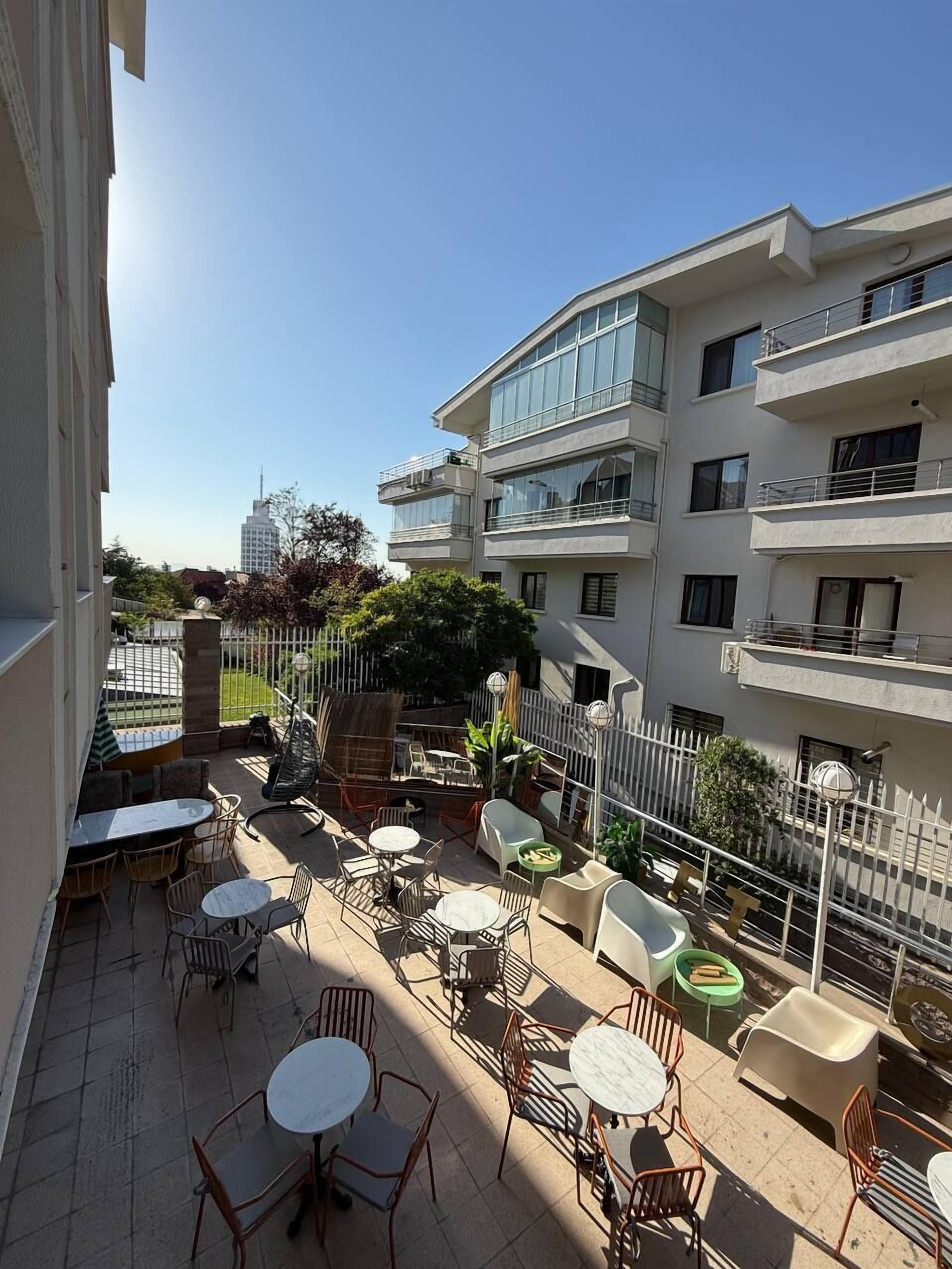 Un immeuble résidentiel à plusieurs étages doté d’une terrasse sur le toit, comprenant un espace de détente extérieur avec des sièges et une petite piscine.