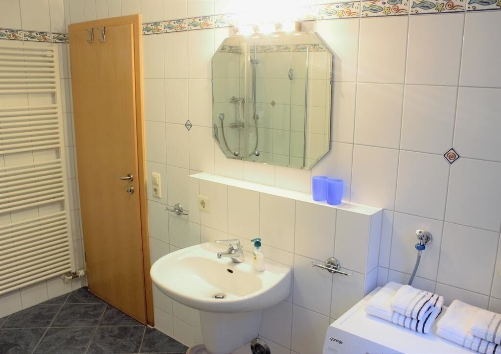 Un baño con lavamanos, espejo, ducha y toallero.