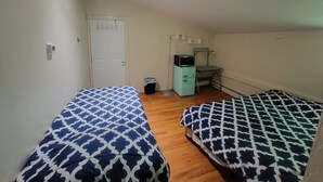 A small, clean room with two beds, a desk, a chair, and a trash bin.