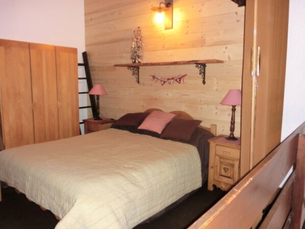 Une chambre à coucher avec une tête de lit en bois, un lit recouvert d’une courtepointe, deux tables de chevet avec des lampes et une étagère murale agrémentée d’un objet décoratif.