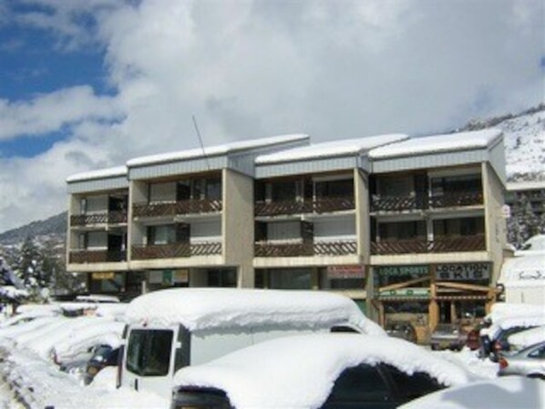 A multi-story building with balconies, surrounded by snow-covered cars.