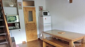 A room with a wooden table, a wooden bench, a white refrigerator, a microwave, a wooden door, and a small shelf with a picture frame. - Duplex 6 Guests, Near Ski Slopes, Balcony, Pet-Friendly (Saint-Chaffrey)