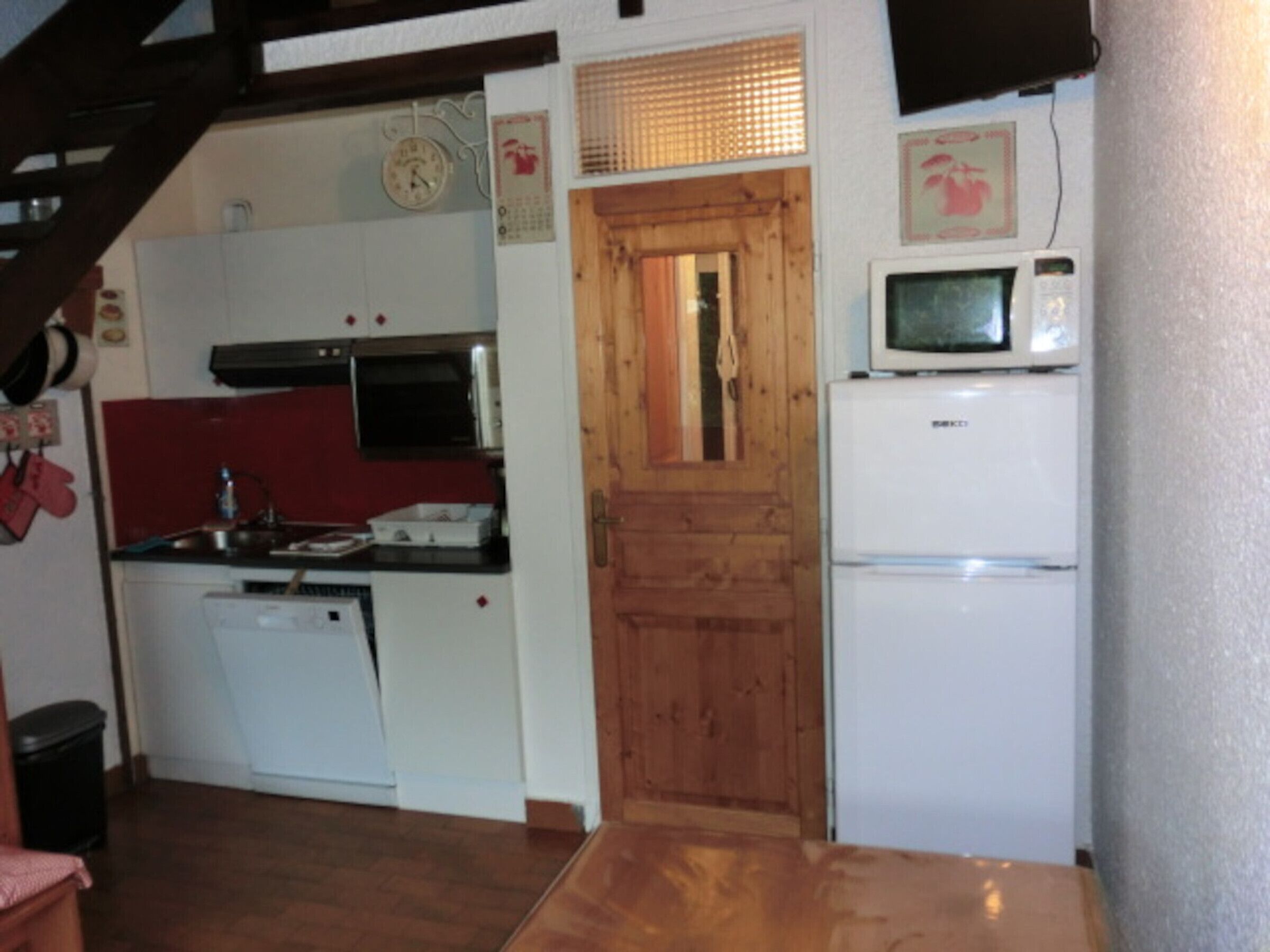 Una cocina compacta con puerta de madera, microondas y refrigerador blanco.