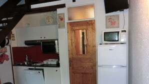 A compact kitchen with a wooden door, a microwave, and a white refrigerator. - Duplex 6 Guests, Near Ski Slopes, Balcony, Pet-Friendly (Saint-Chaffrey)
