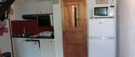 Una cocina compacta con puerta de madera, microondas y refrigerador blanco.