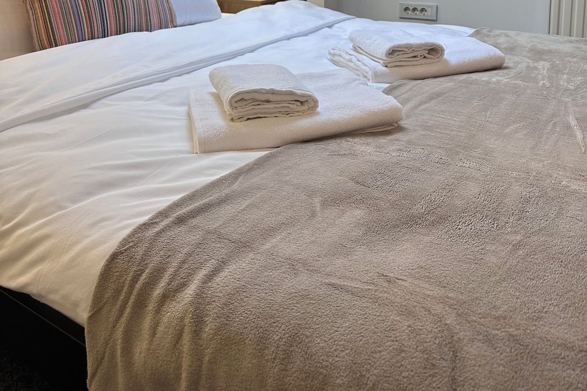 Un lit bien fait, avec des serviettes, une lampe de chevet et une lucarne au-dessus.