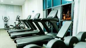 A row of treadmills and dumbbells in a gym with large windows and a view of a cityscape at night. - The Moon Apartment-Luxurious modern 2-bedroom apartment in Kigali (Kigali)