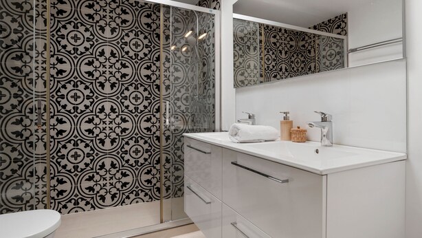 Un baño moderno con pared estampada, lavamanos blanco y cabina de ducha de vidrio.