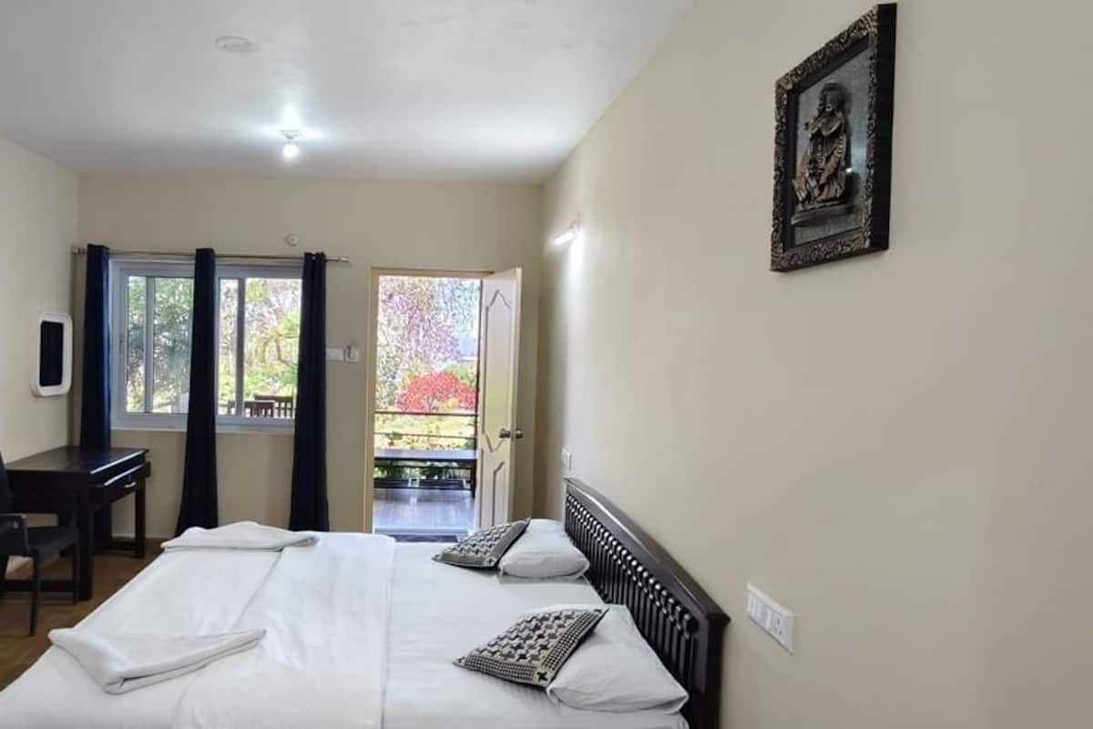 A bedroom with a bed, a desk, a chair, a TV, and a balcony with a view of trees.