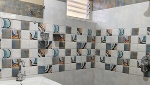 Een badkamer met een wastafel, betegelde wanden, een raam en een blauwe bak.