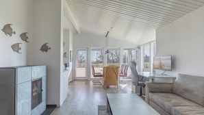 En moderne stue med pejs, sofa, spiseområde med stole og et fjernsyn.