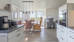 Et moderne køkken med spiseplads, store vinduer og udsigt til naturen.