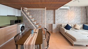 A modern kitchen with a microwave, toaster, and sink, a dining area with a table and chairs, and a living area with a sofa and cushions.