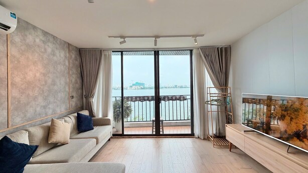 A modern living room with a sofa, a TV, and a view of a body of water through large glass doors.