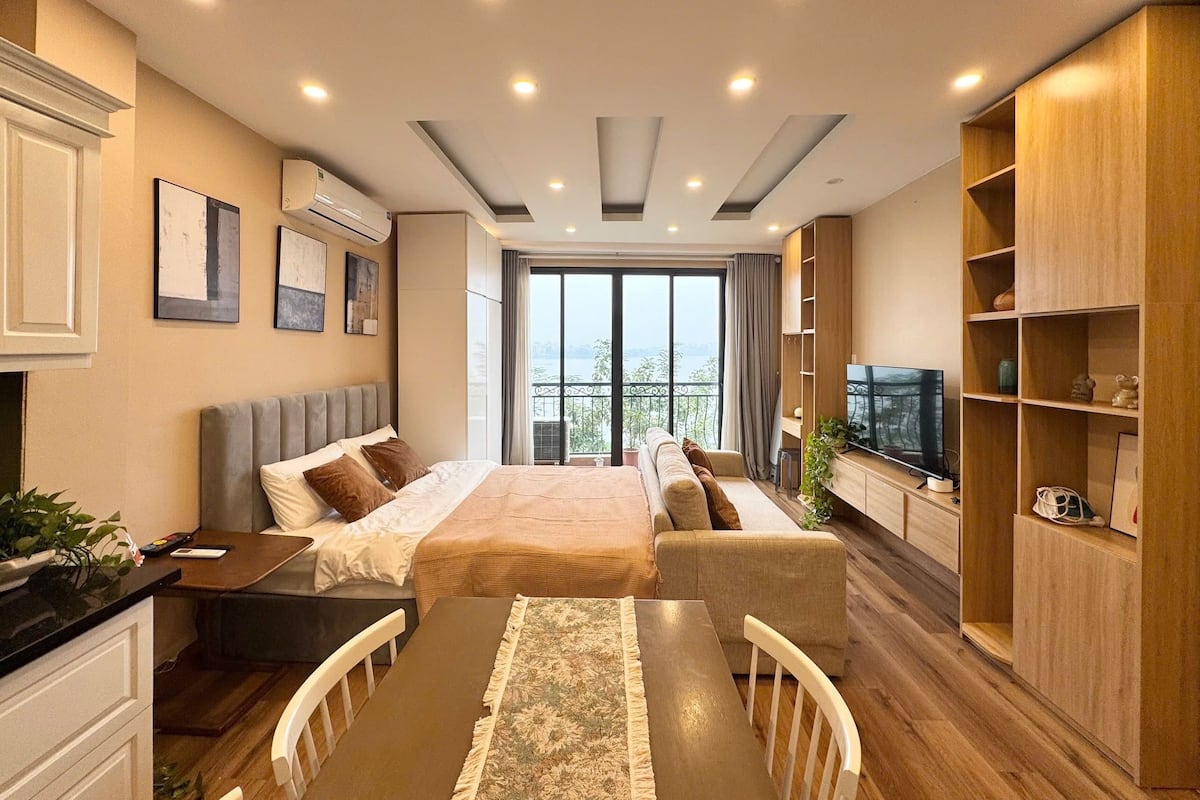A modern bedroom with a bed, bedside tables, a TV, and a balcony with a view.