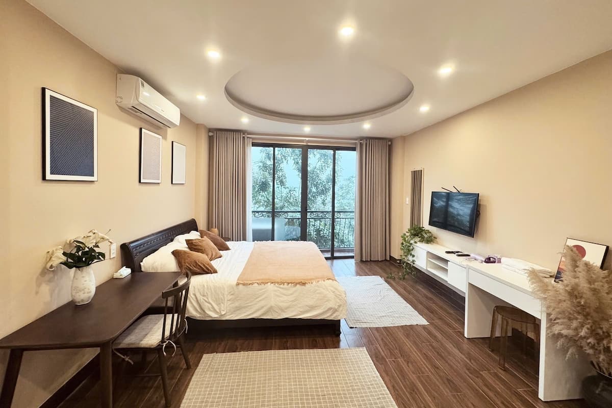 A modern hotel room with a large bed, a desk, a TV, and a balcony with a view.