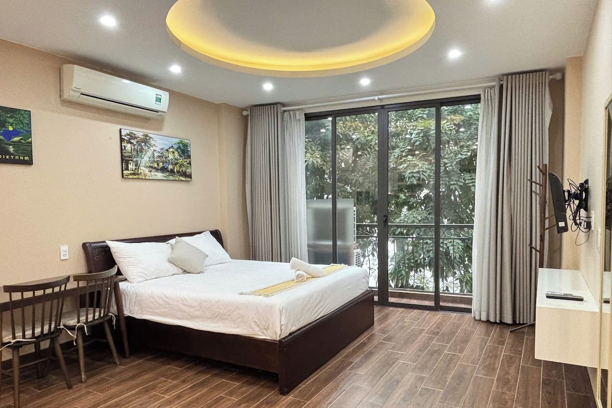 A hotel room with a bed, a desk, a chair, a TV, and a balcony with curtains.