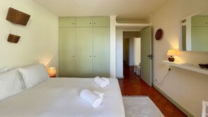 A bedroom with a bed, two towels, a nightstand, a lamp, a wardrobe, and a mirror.