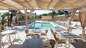A poolside area with lounge chairs, tables, and umbrellas providing shade. - Linari Sea & Suites (Ormos Panagias)