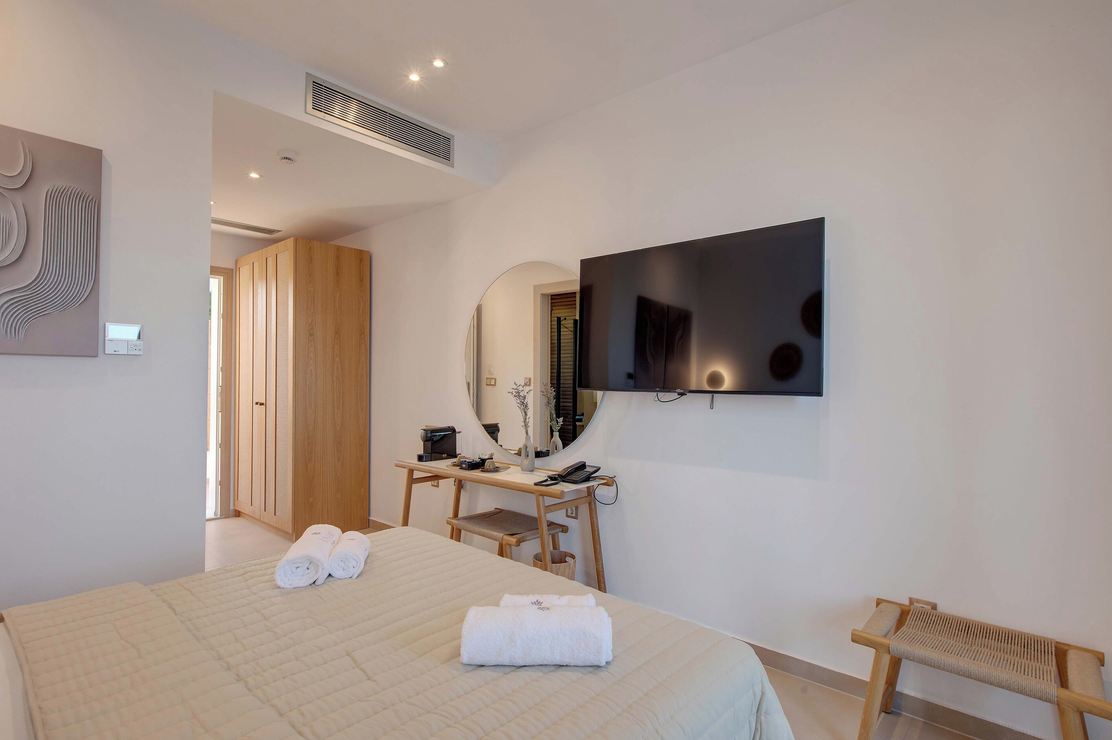 Een moderne hotelkamer met een groot bed, een bureau met stoel, een aan de muur bevestigde televisie en een houten kledingkast.