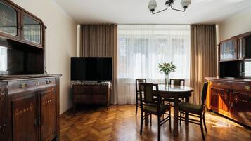 Una habitación con piso de madera en parquete, una mesa de comedor con sillas, un televisor y un mueble con espejo.