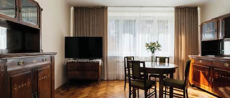 Una habitación con piso de madera en parquete, una mesa de comedor con sillas, un televisor y un mueble con espejo.