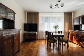 A room with a wooden herringbone floor, a dining table with chairs, a television, and a cabinet with a mirror. - Native Apartments Fałata 12 (Kraków)