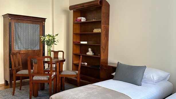 A bedroom with a bed, two chairs, a wooden cabinet, and a ceiling light fixture. - Native Apartments Fałata 12 (Kraków)