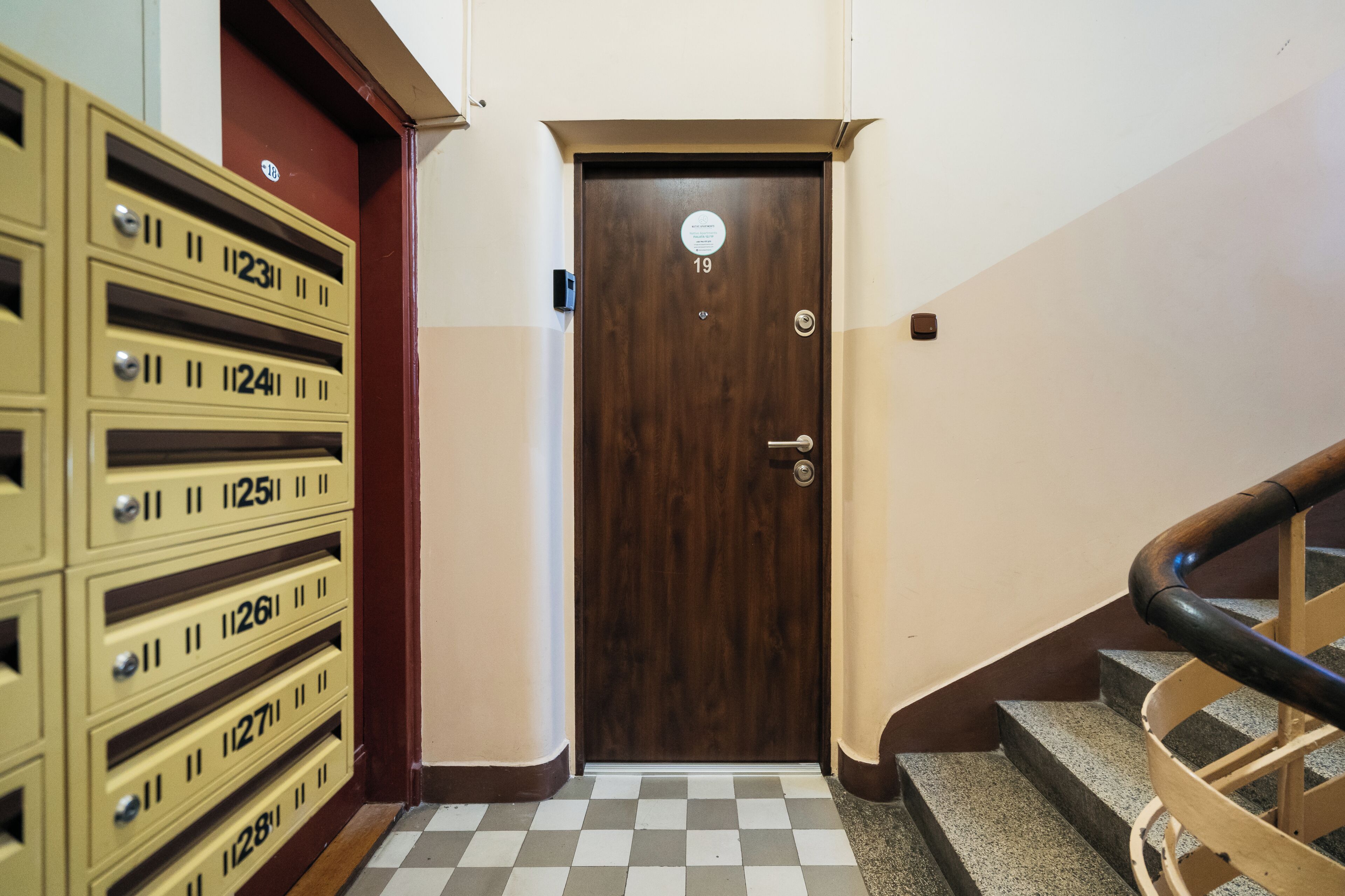 Habitación de hotel con puerta de madera, piso a cuadros y escalera con barandilla de madera.