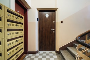 A hotel room with a wooden door, a checkered floor, and a staircase with a wooden handrail.