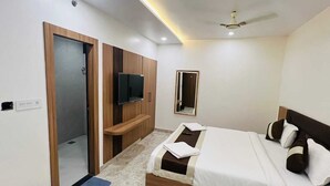 Une chambre à coucher avec un lit, un téléviseur fixé sur un meuble en bois, un ventilateur de plafond et un petit miroir au mur.