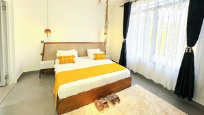Ein Schlafzimmer mit einem großen Bett, einem Nachttisch, einer hängenden Leuchte und Blick durch durchscheinende Vorhänge.