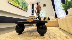 Ein modernes Wohnzimmer mit einem großen Gemälde, einem schwarzen Couchtisch mit Büchern, einer Couch und einer Topfpflanze.