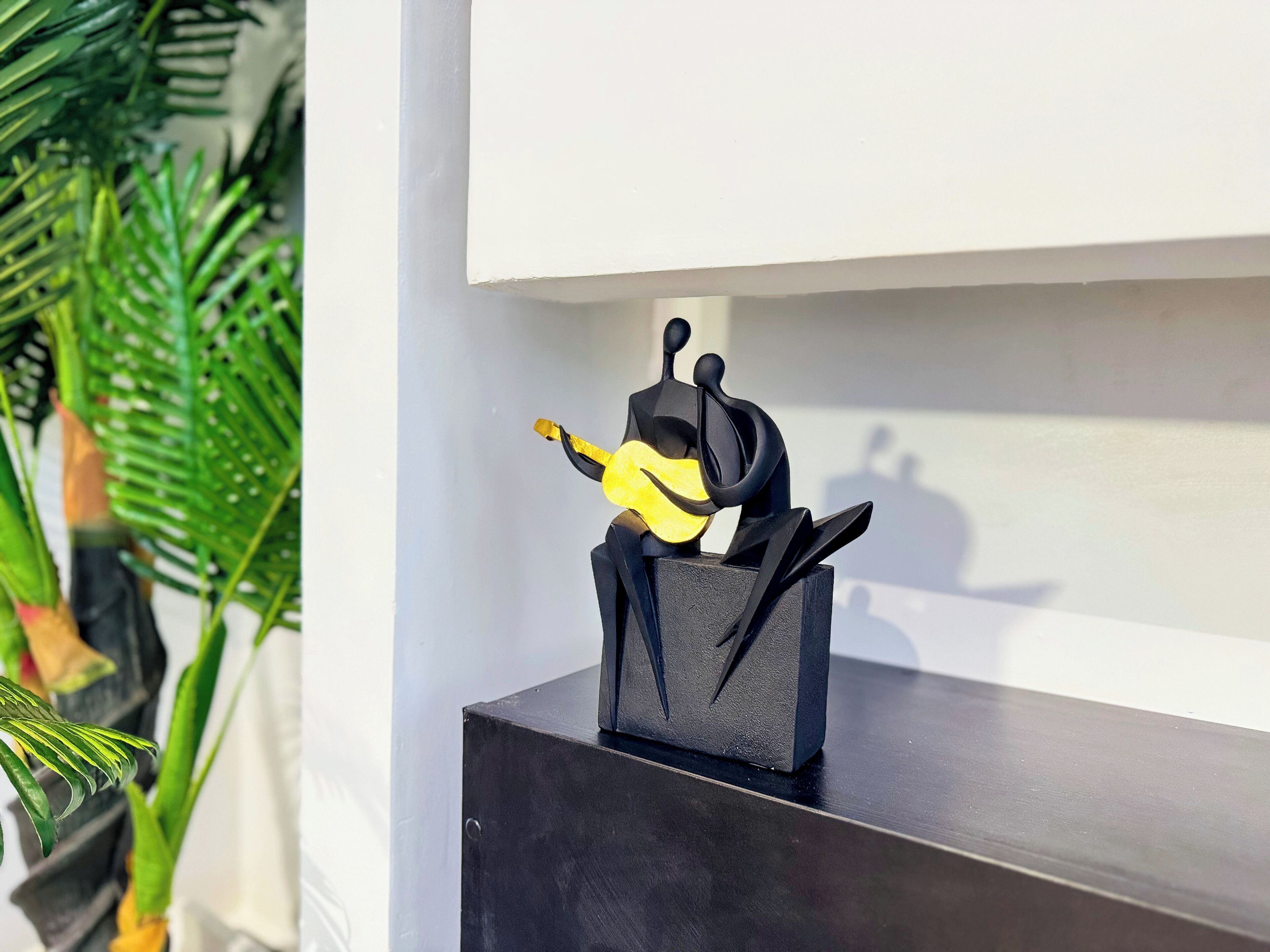 Una escultura negra de una figura tocando la guitarra sobre un estante de madera oscura.