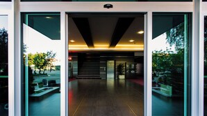A modern building entrance with glass doors, a wooden floor, and a staircase leading inside.