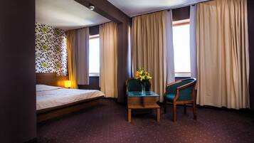A hotel room with a bed, a desk with a vase of flowers, a chair, and curtains.