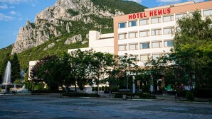 A hotel named 'HOTEL HEMUS' with a modern building, a fountain, and a mountainous backdrop.