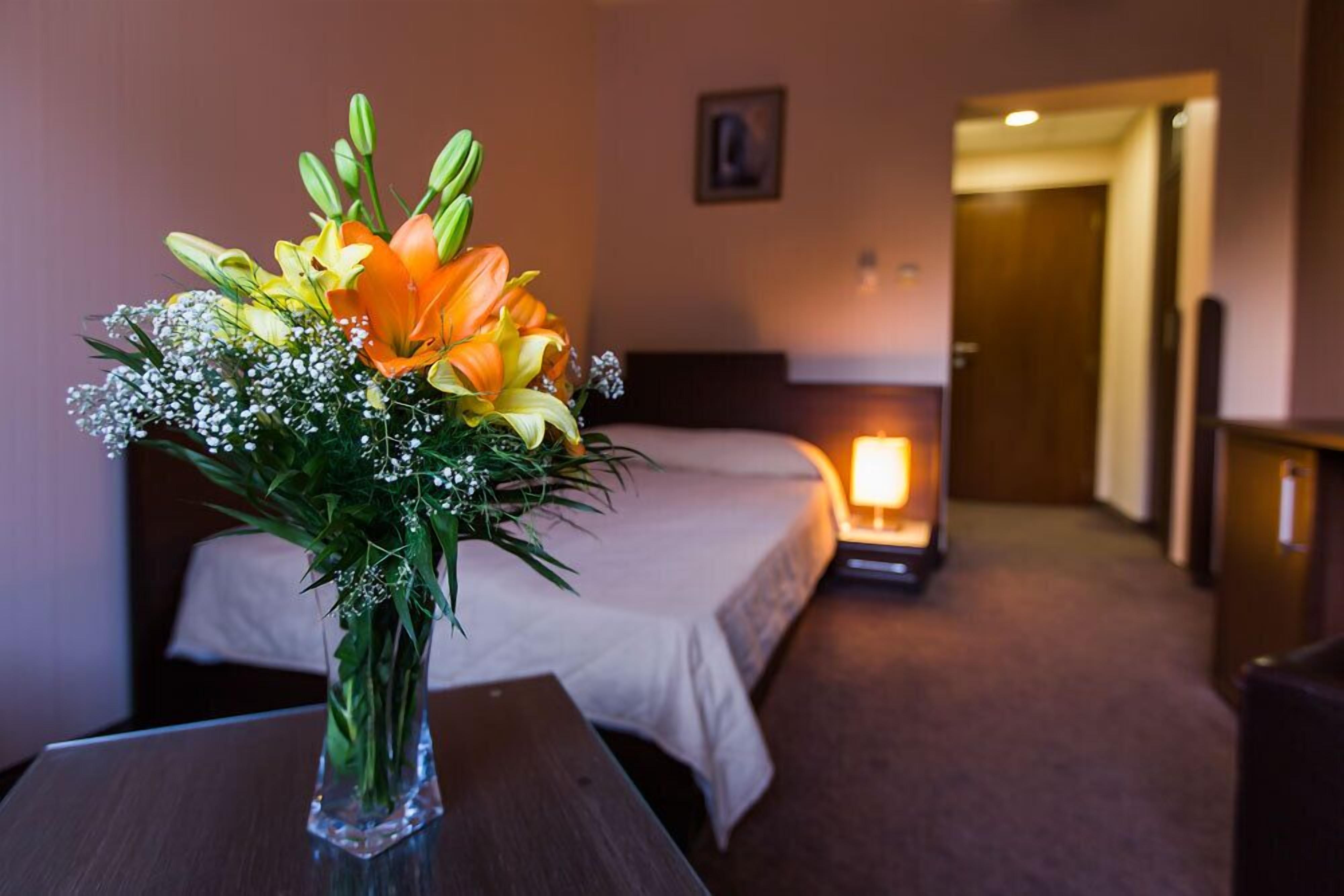 Ein Hotelzimmer mit einem Bett, einem Nachttisch mit Blumenvase und einer beleuchteten Nachttischlampe.