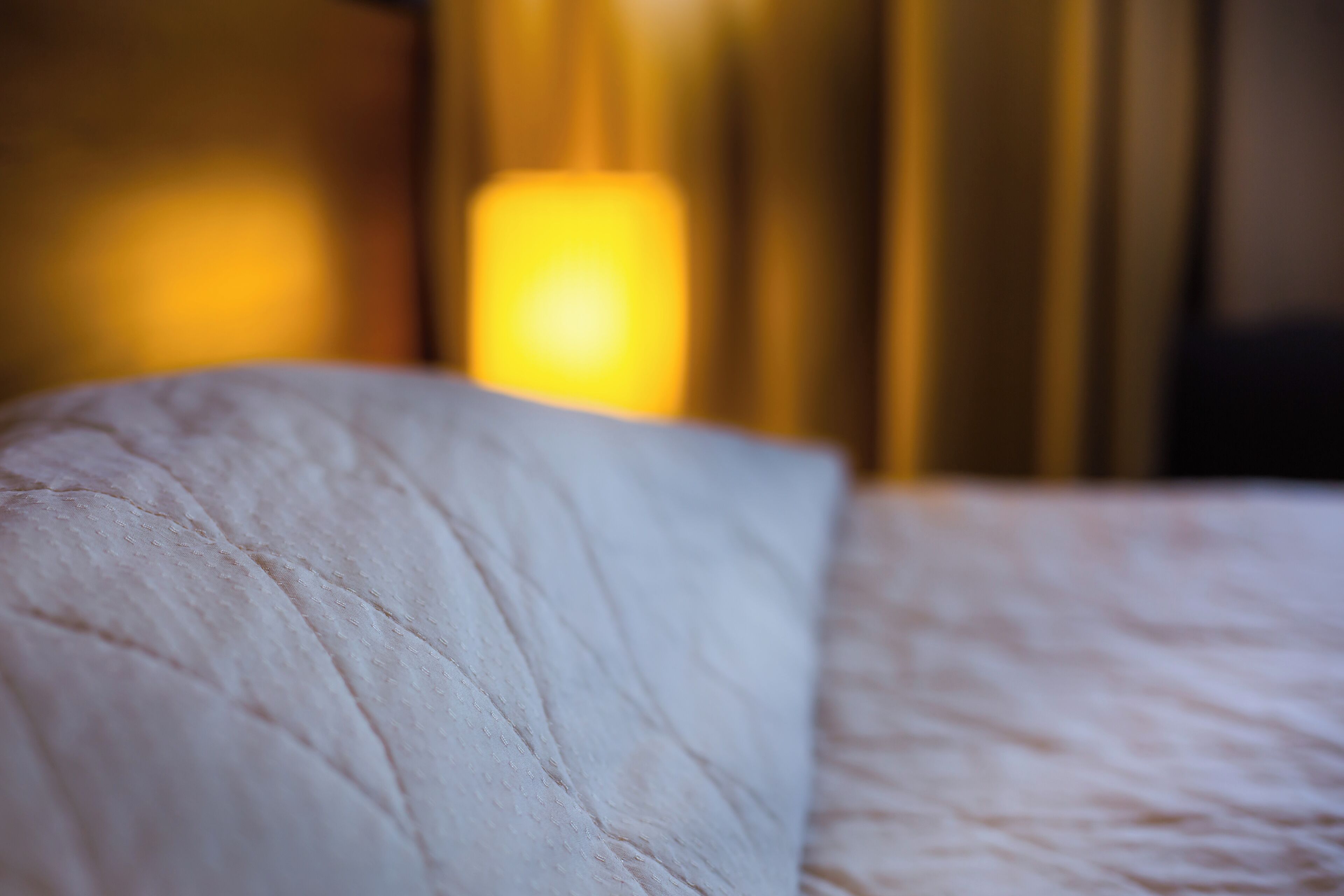 A close-up of a bed with a white pillow and a textured blanket.