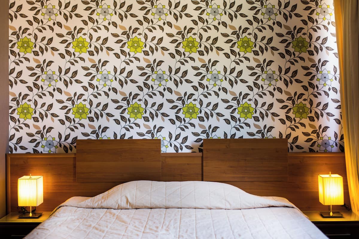 Una cama con cabecera de madera, dos lámparas de noche y un estampado floral en el papel tapiz.