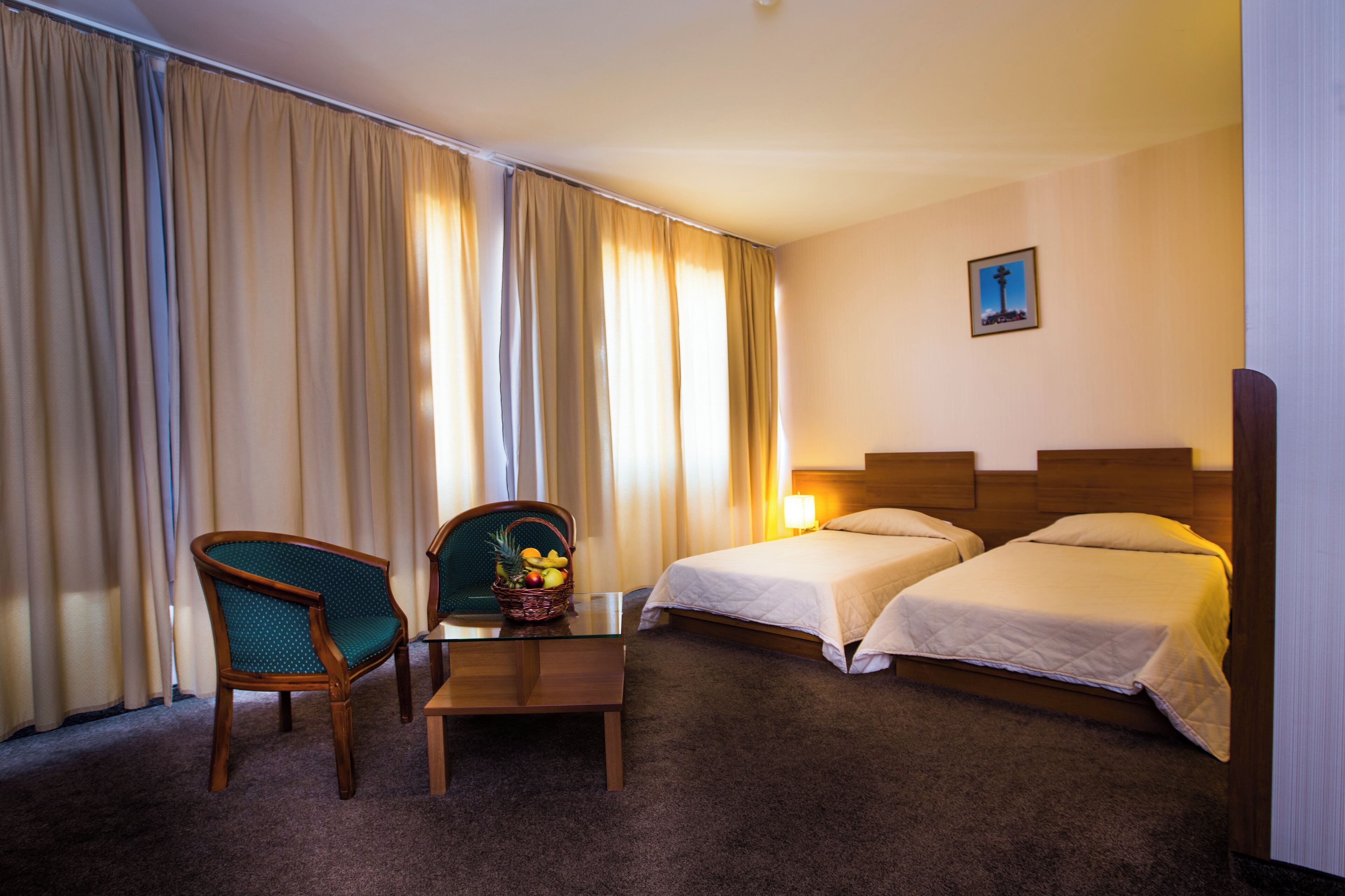A hotel room with two beds, a desk with a chair, and a small table with a fruit basket.