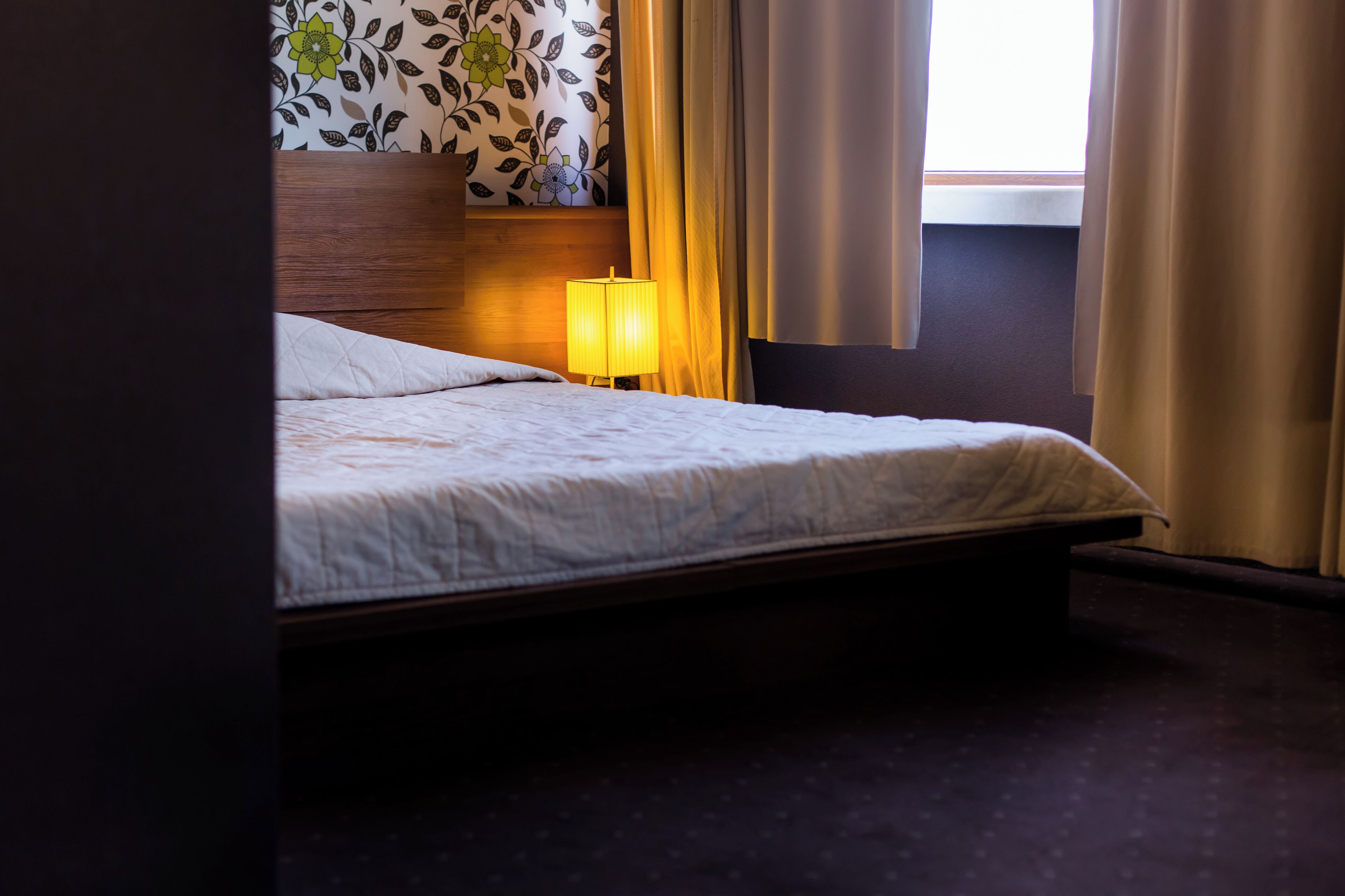 A single bed with a wooden headboard, a bedside lamp, and a window with curtains.