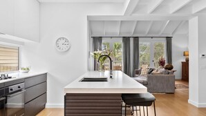Et moderne køkken med en central ø, et spiseområde med en sofa og udsigt til det fri.