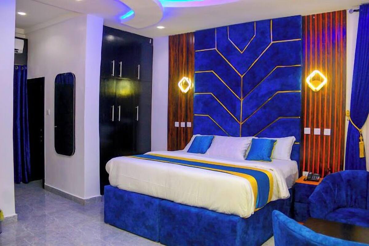 A modern hotel room with a large bed, a blue accent wall, and a unique geometric design on the headboard.