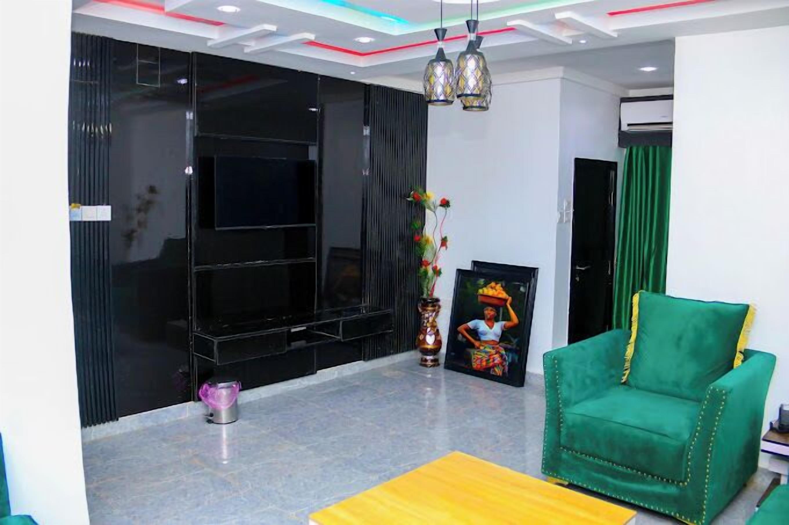 A modern living room with a flat-screen TV, a green armchair, a vase with flowers, and a framed picture on the wall.